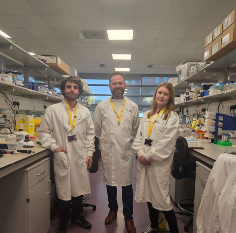 Dr Niall Kenneth and his team in lab coats in their lab, with Worldwide Cancer Research lanywards