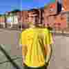 Sam poses in yellow Worldwide Cancer Research t-shirt on a cobble street in front of red brick buildings